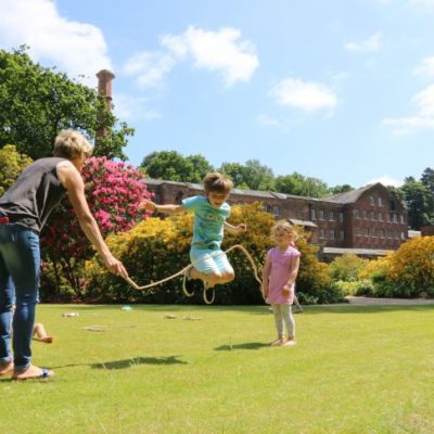 Two small children and their guardian have fun skipping in a large garden.