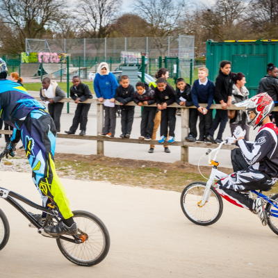 Two young BMXers ride around a BMX track in front of a crowd