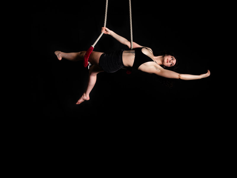 A woman hangs from ropes showing circus skills
