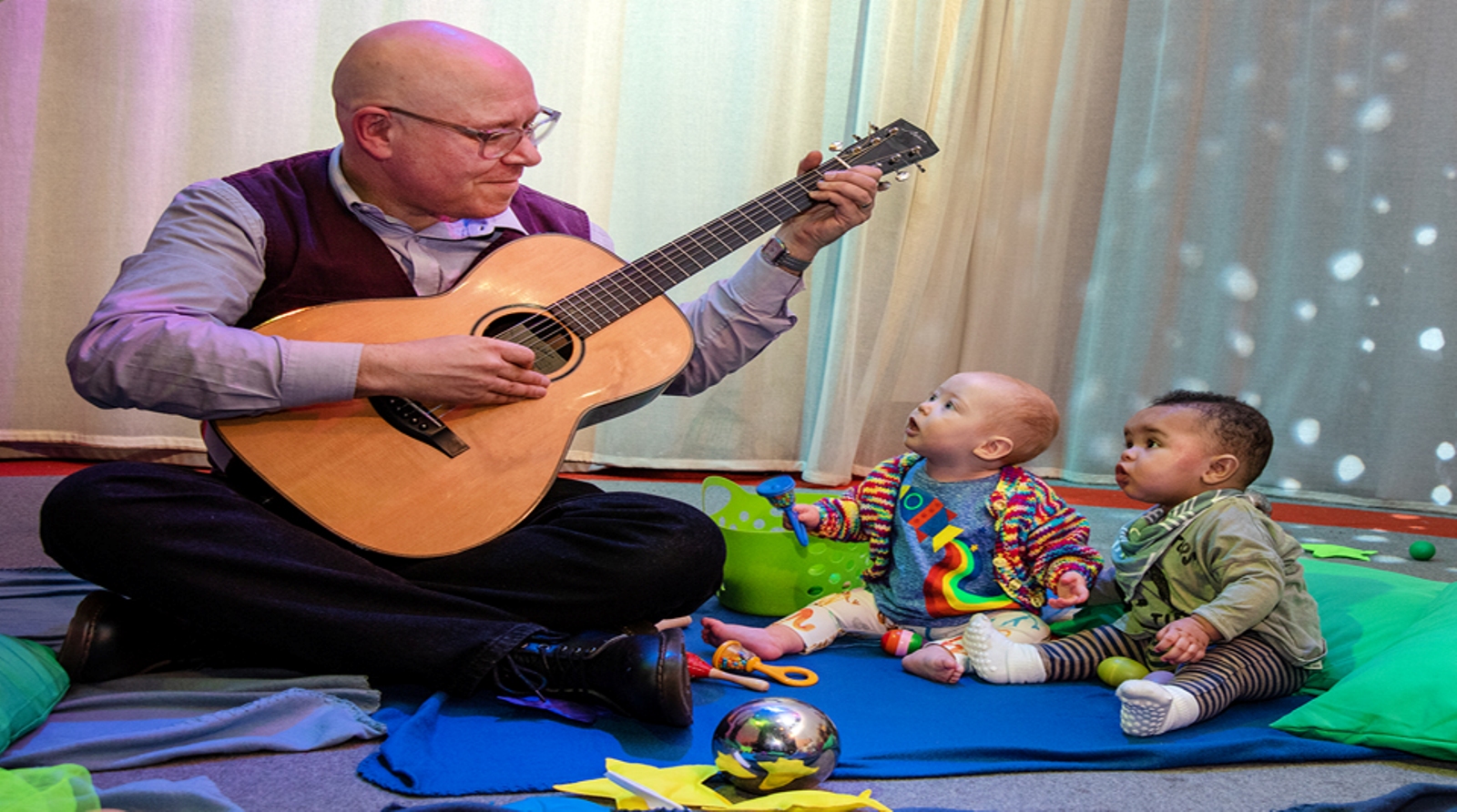 Man sat down playing his guitar to two toddlers