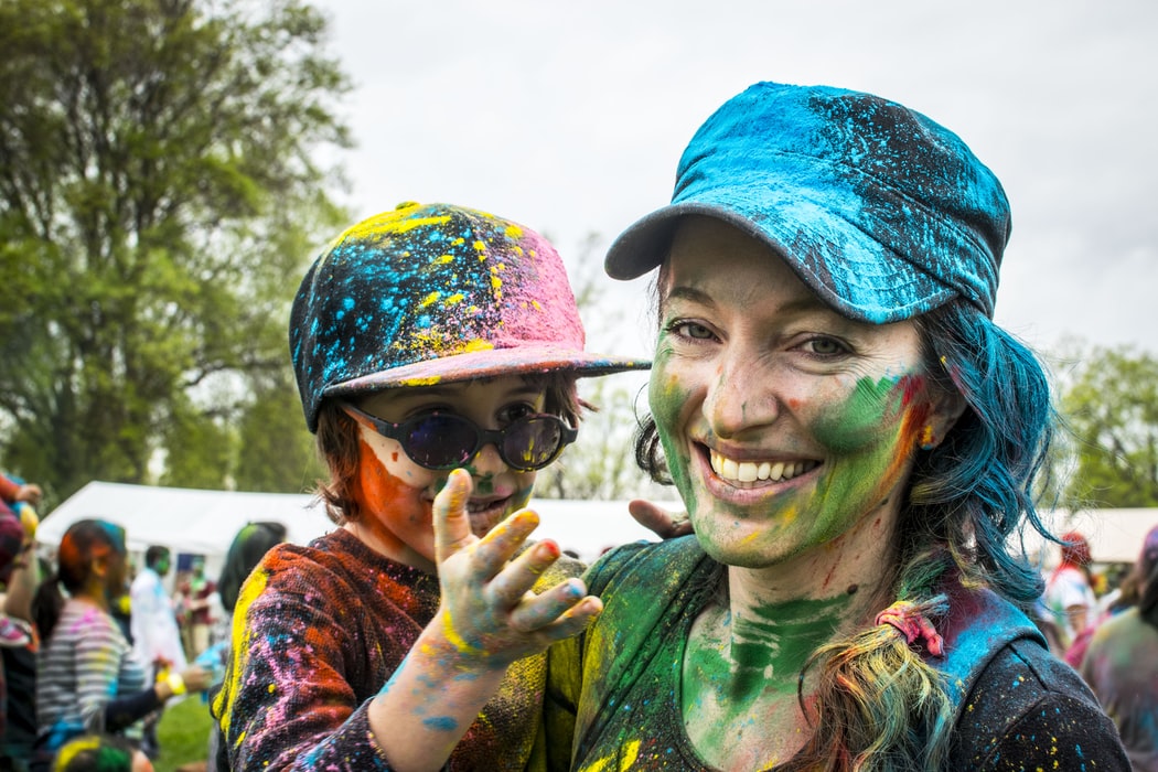 A mother holds her child in her arms. Both of them are covered in brightly coloured paint.