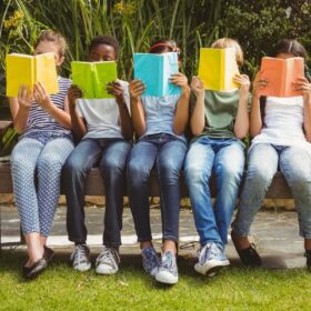 Five children sitting on a bench reading books with bright covers