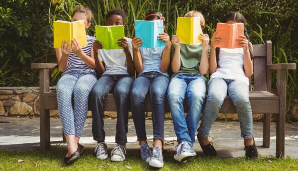 Five children sitting on a bench reading books with bright covers