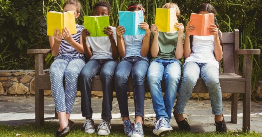 Five children sitting on a bench reading books with bright covers