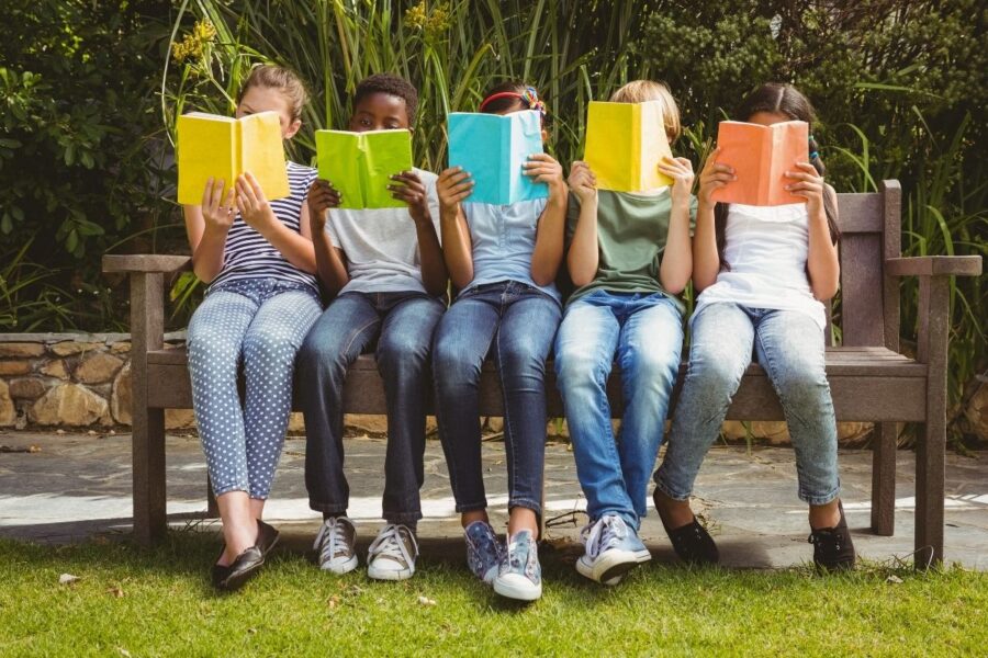 Five children sitting on a bench reading books with bright covers
