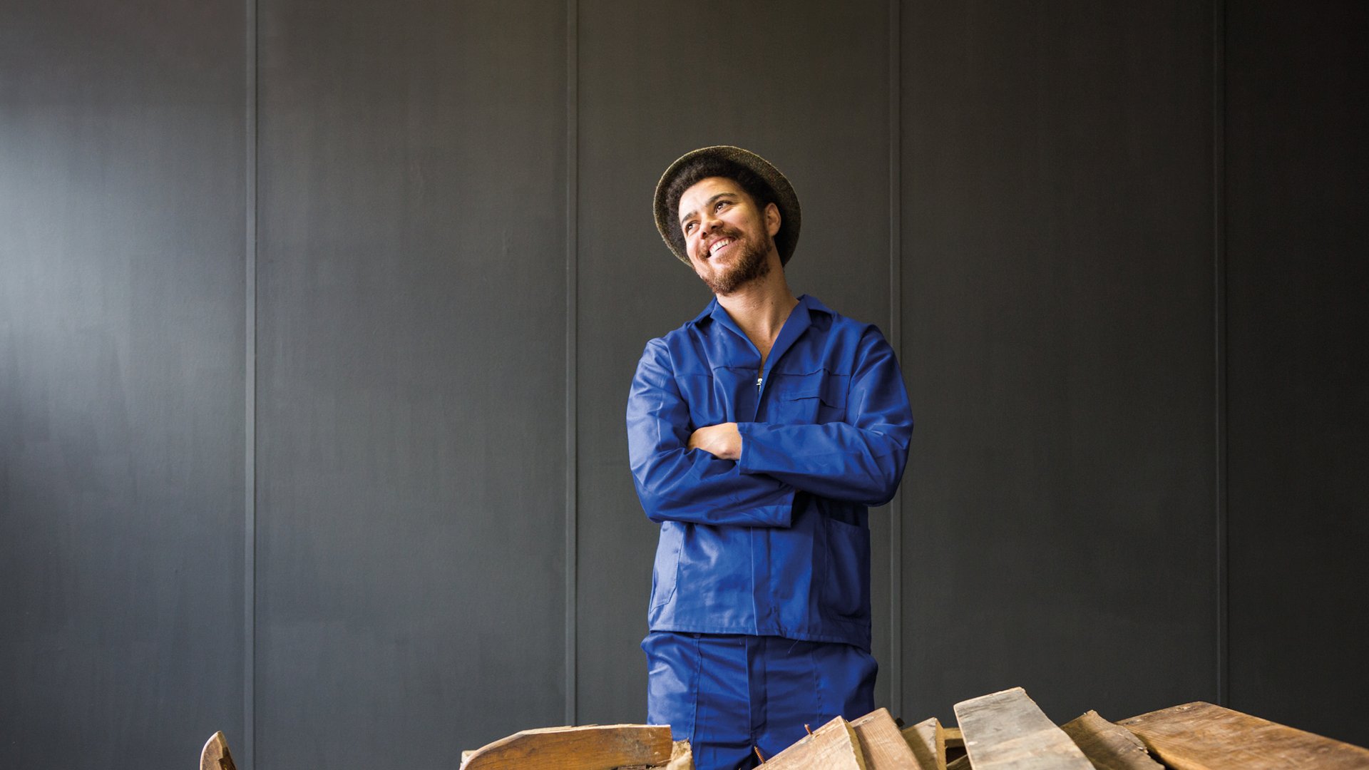 South African artist Kemang Wa Lehulere stands smiling, wearing a blue suit and a brown hat.