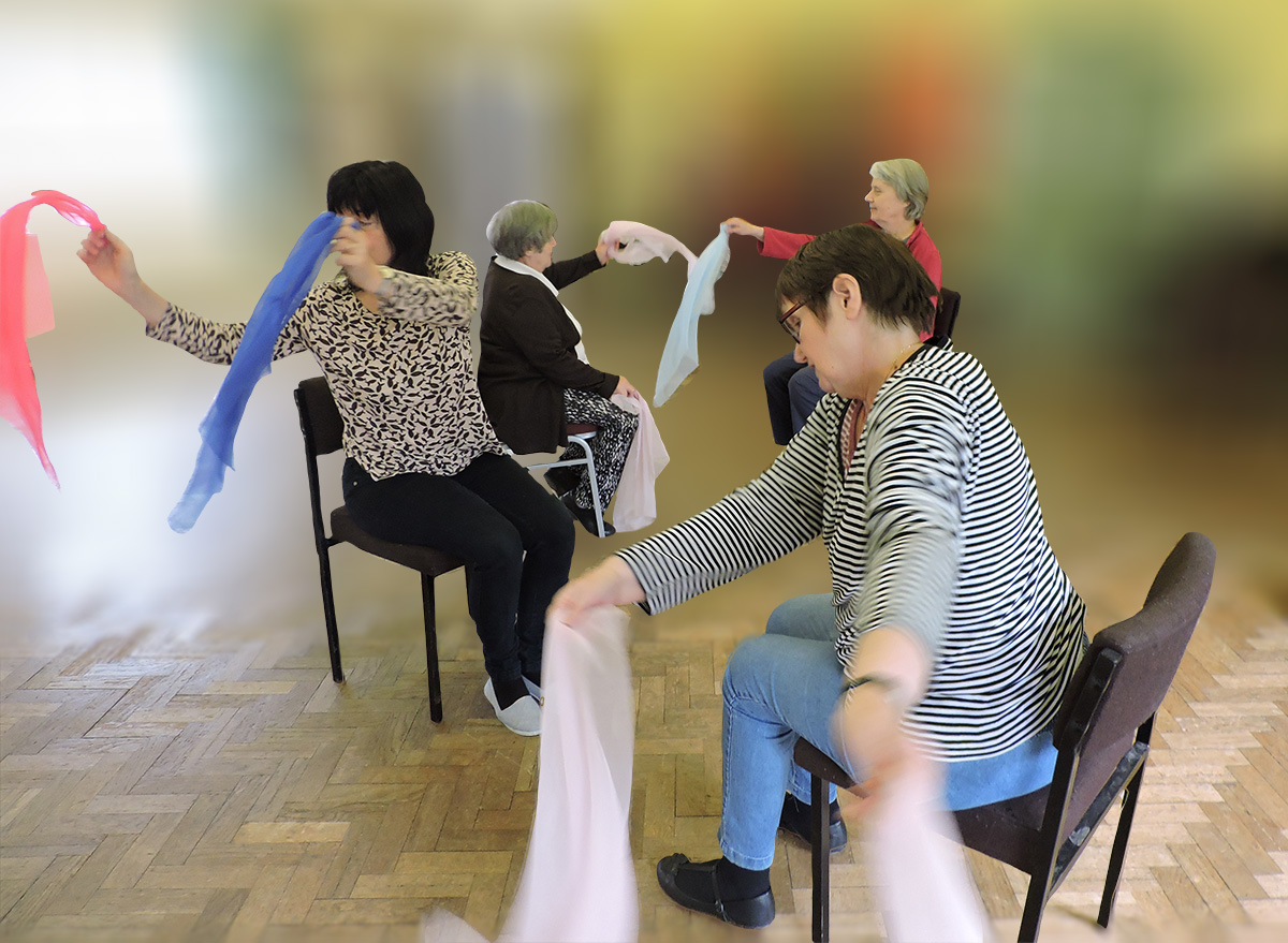 A small group of people enjoying chair dancing with brightly coloured scarves.