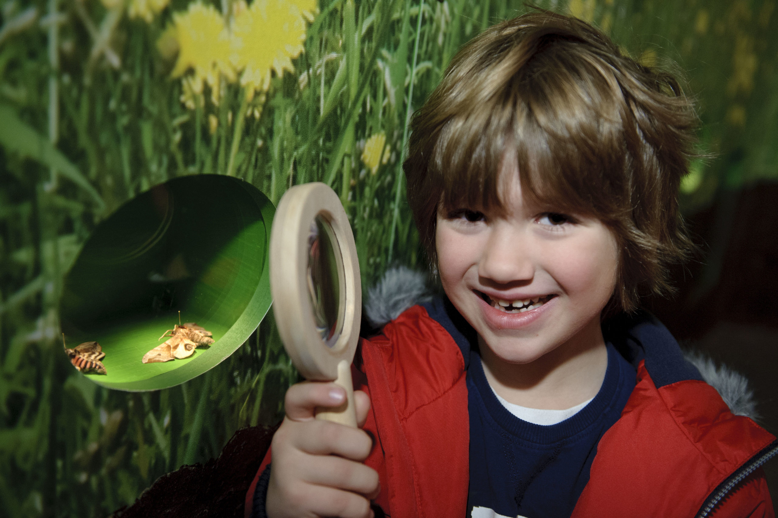 An enthusiastic young child stands in a museum holding a magnifying glass.