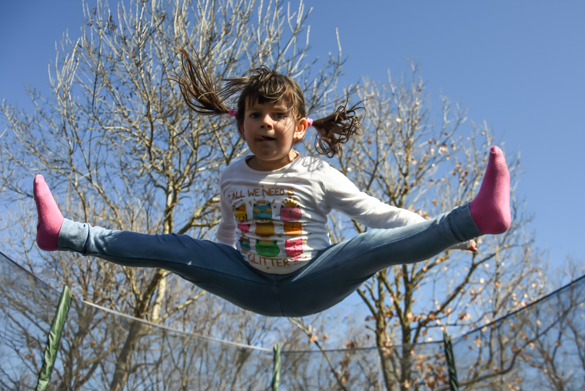 A small girl jumps high on her trampoline.