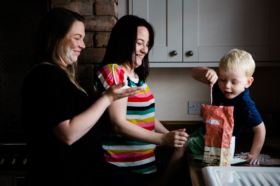 A family of two mums and a toddler have fun baking in a kitchen.