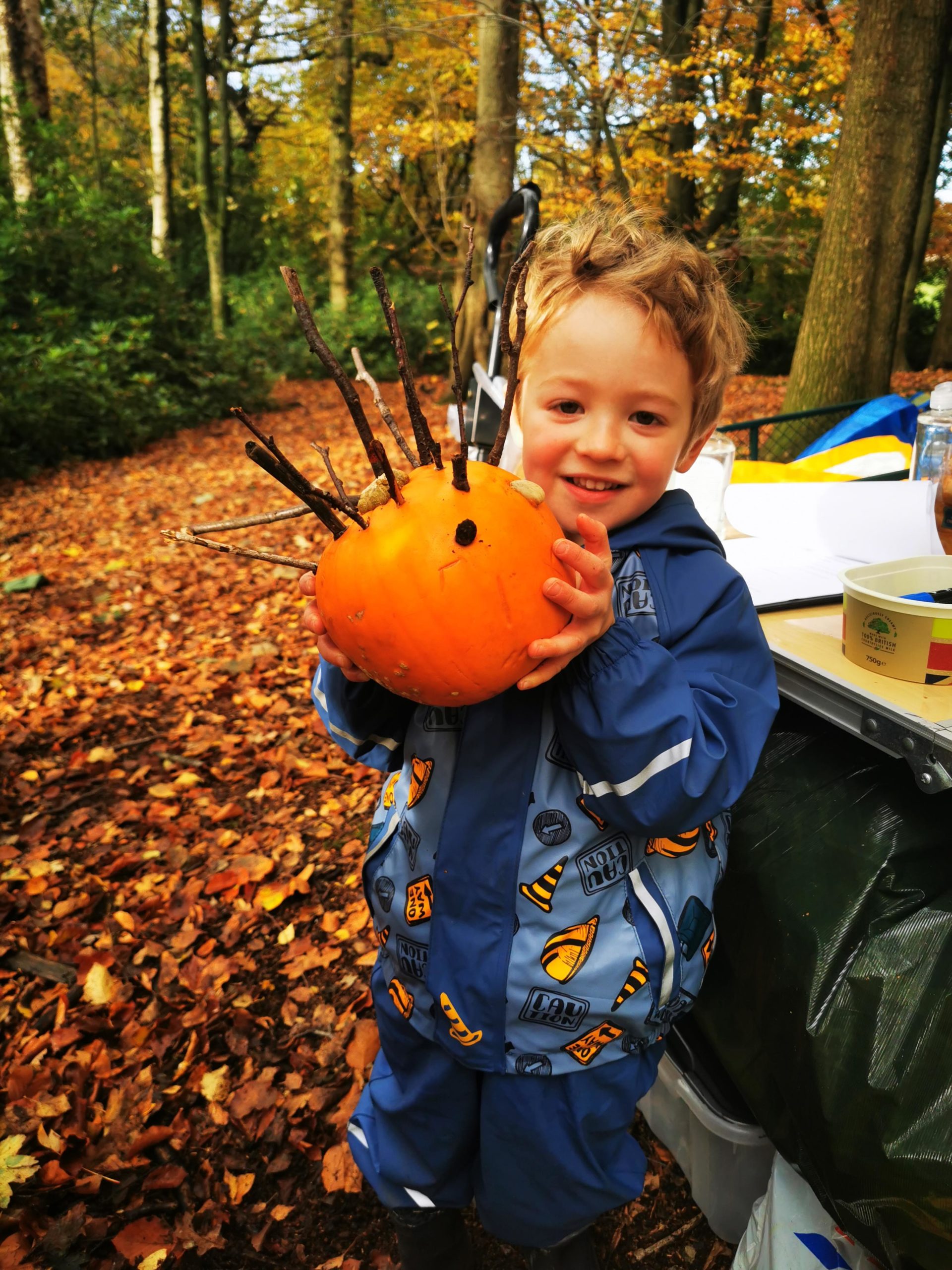 a child holds up a pumpkin in a forest.