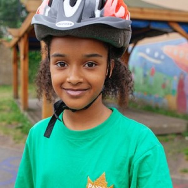A young person stands wearing a cycle helmet.