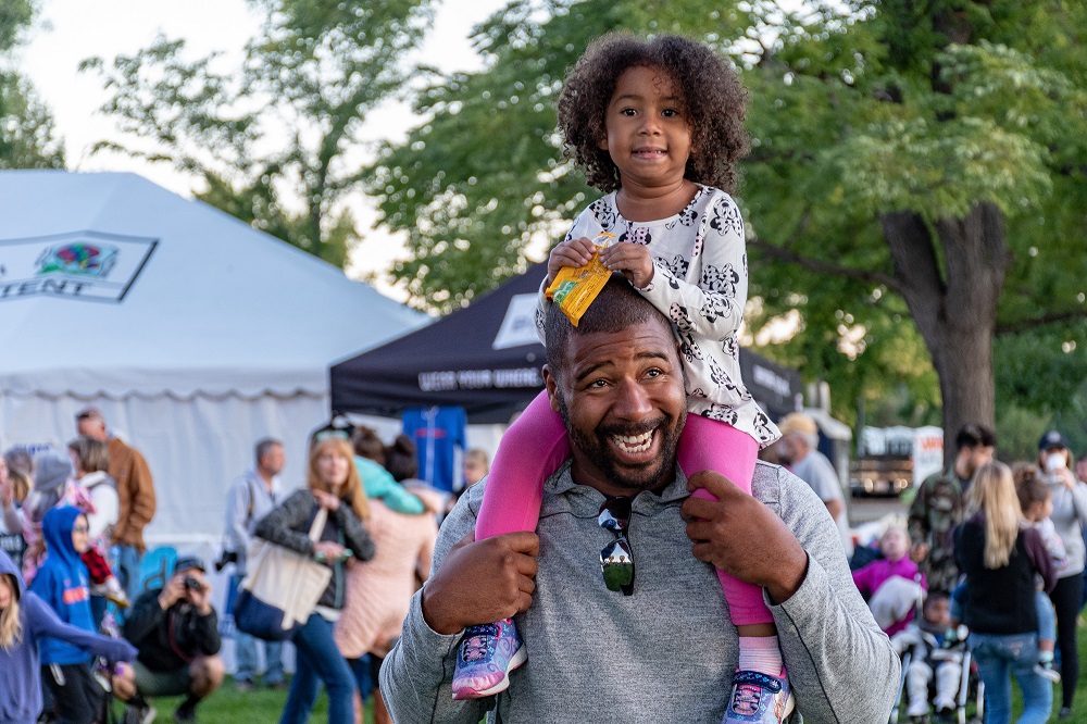 A small child sits on the shoulders of an adult at a festival.