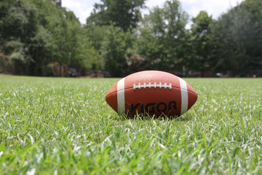 An american football sits on a grassy pitch.