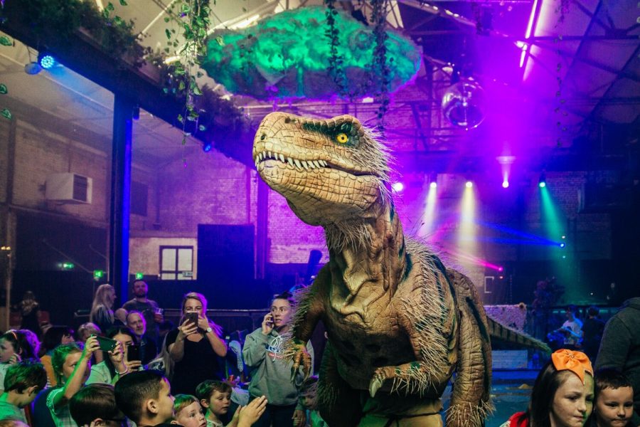 A life-size model of a T-Rex stands in front of a live audience.