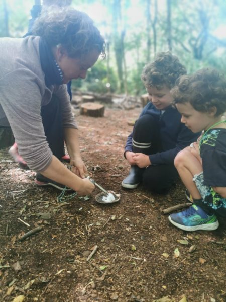 An adult and two small children craft in the woods.