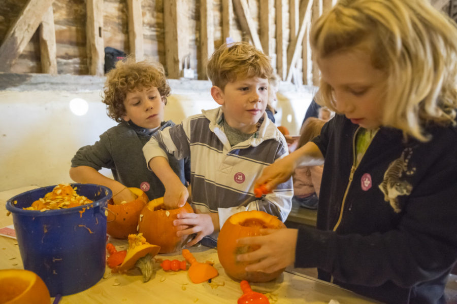 Three children carve out pumpkins together on a table.