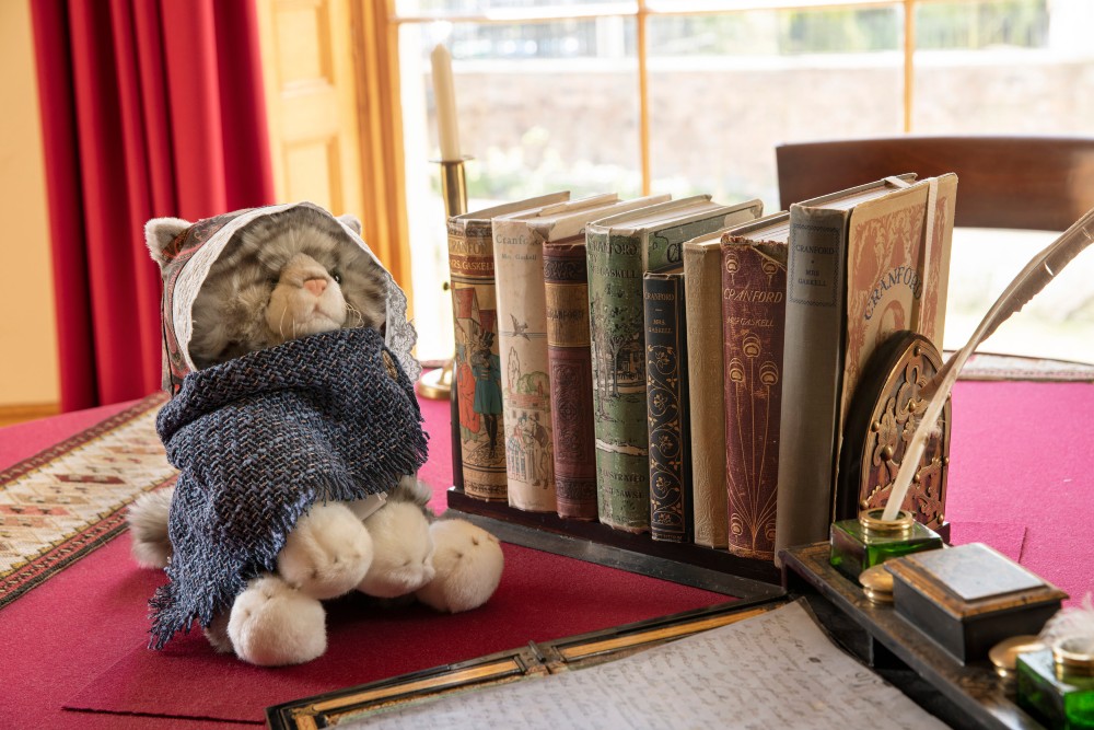 A window ledge full of books and a cat plush toy placed next to it.