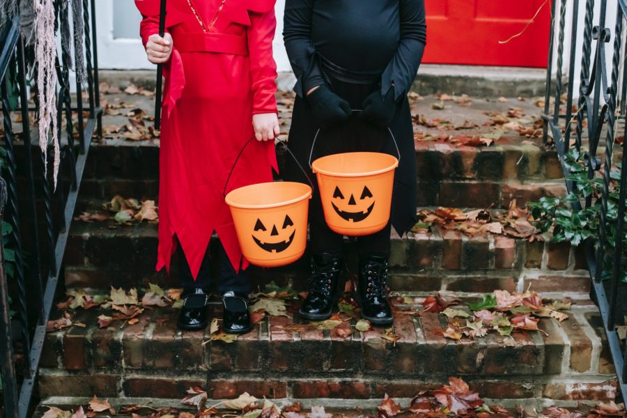Two children, dressed up for Halloween, stand holding trick or treat buckets.
