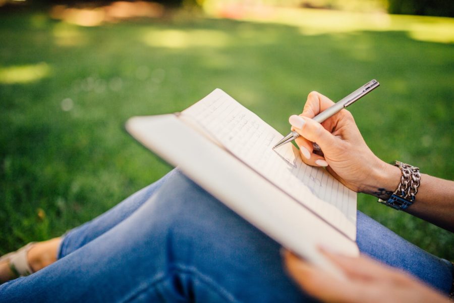 A person sits outside on the grass and writes in a note book.