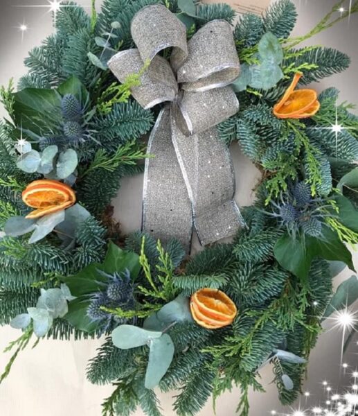 A Christmas wreath with orange slices, eucalyptus and a silver bow on it.