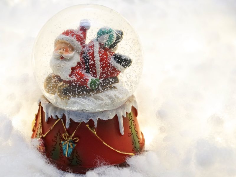 A snow globe with a red base and a jolly Father Christmas figure sits in the snow.