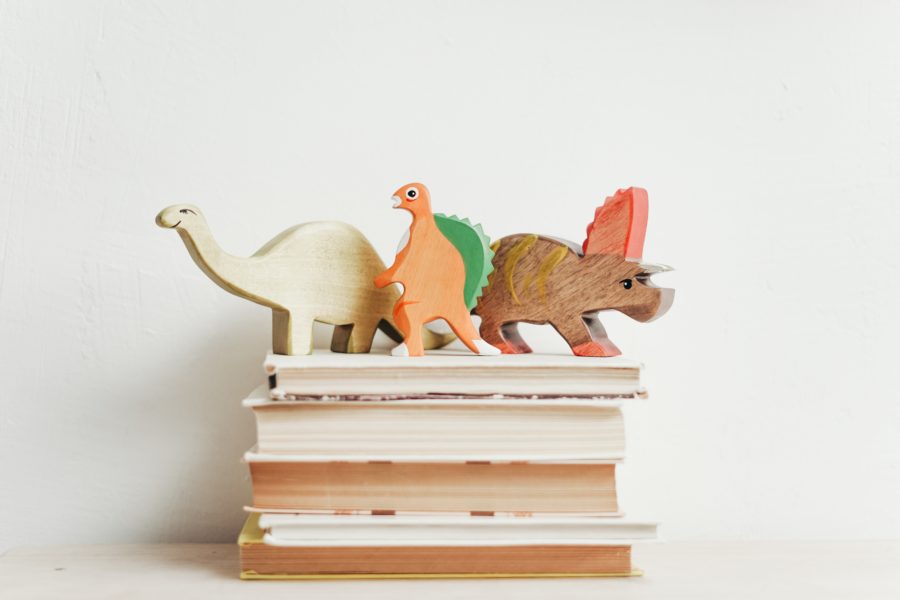 Three wooden dinosaurs on top of a pile of books