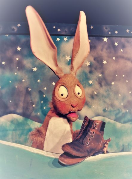 A rabbit puppet looks surprised and holds an old boot.