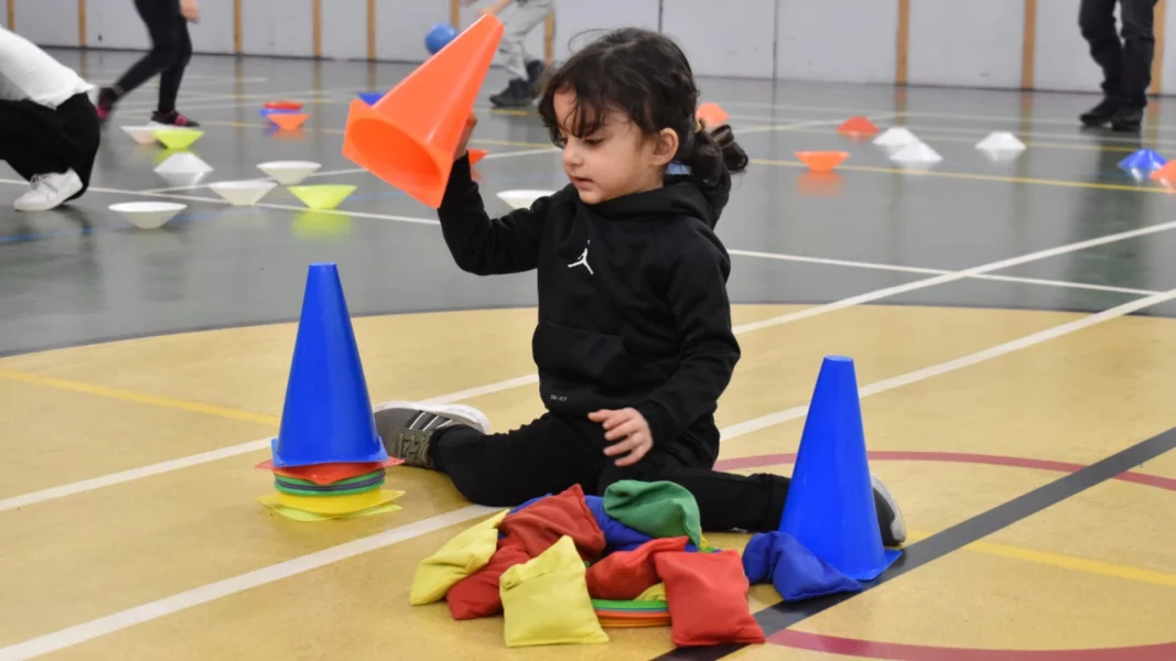 A small child plays with training cones in a sports hall