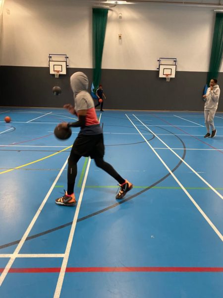 A young person plays basketball in a sports hall