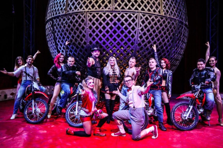 The circus funtasia troupe stand in front of a large metal sphere.