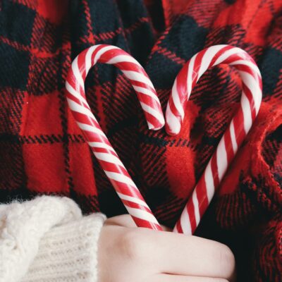A person holds two red and white striped candy canes in their hand making the shape of a heart.