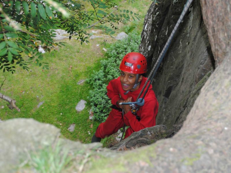 A young person with a red jumpsuit and hardhat abseiling