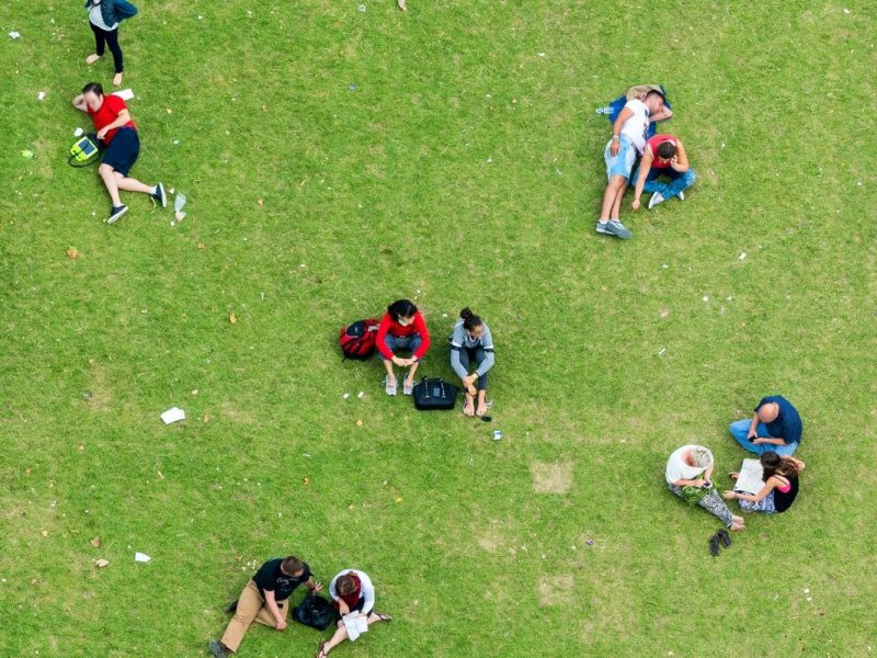 A grassy field with five groups of people sat down on the grass