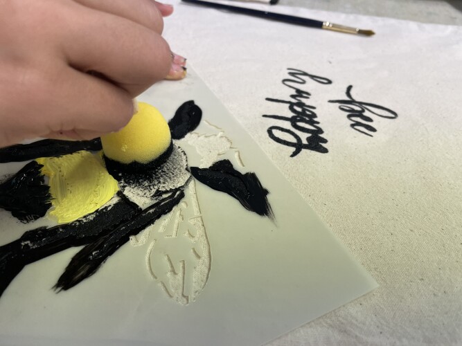 A young person makes a stencil painting of a bee