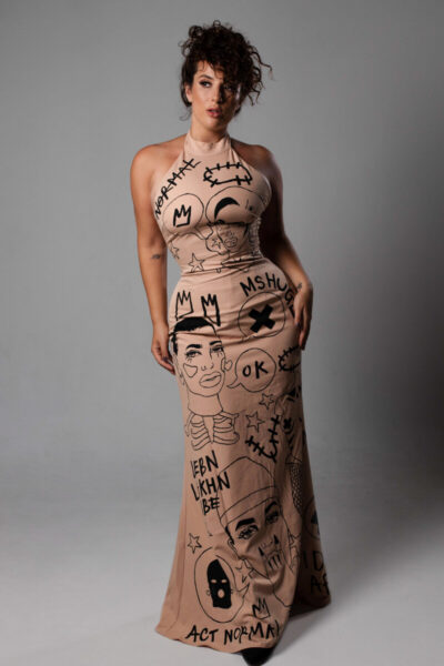 Emma Smith, a white woman with curly brown hair in a long beige dress with black doodles on it