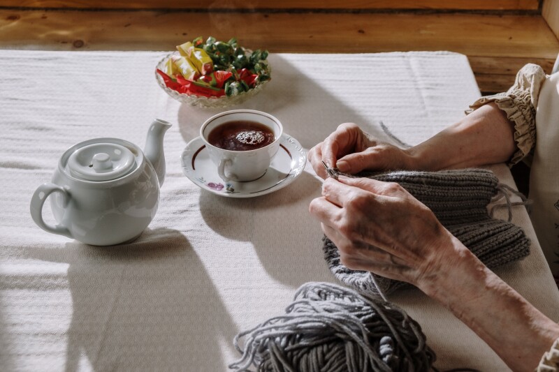 person sitting on a table with a tea pot and cup knitting