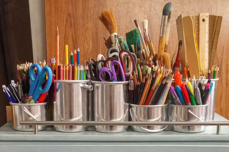 A range of arts and crafts materials, like colouring pencils and paint brushes, in pots.
