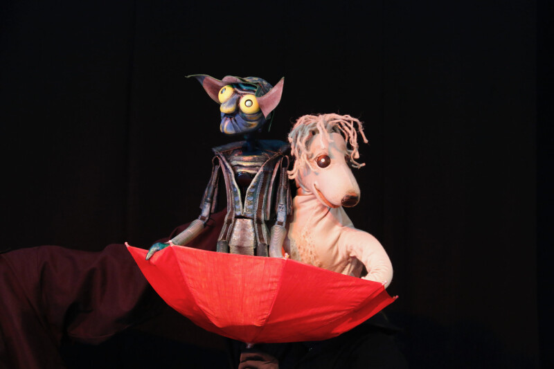 Two puppets, called Flotsam and Jetsam, that look completely different sit onboard an upturned red umbrella.