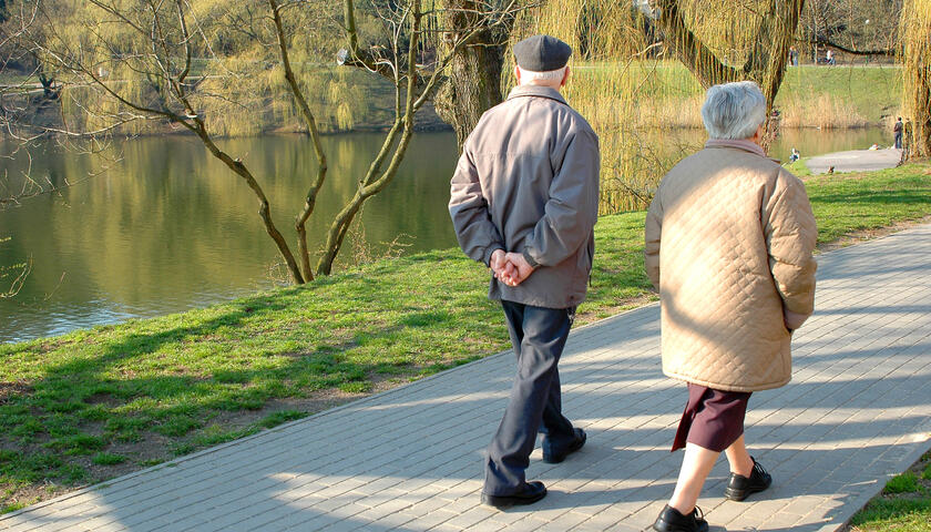 An older couple walking along a pathway at the side of a river.