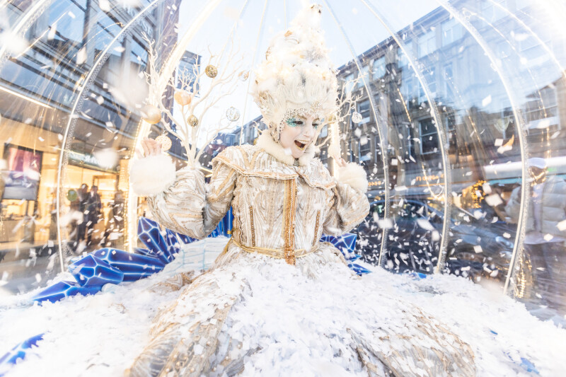 A person dressed up as a snow globe with a large white dress on, a tall white wig and a surprised expression on their face.