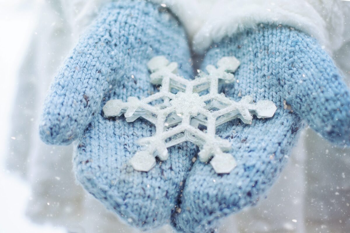 Hands wearing light blue gloves hold a large crafted snowflake.