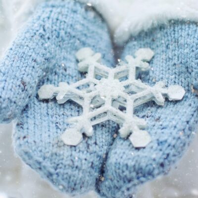 Hands wearing light blue gloves hold a large crafted snowflake.