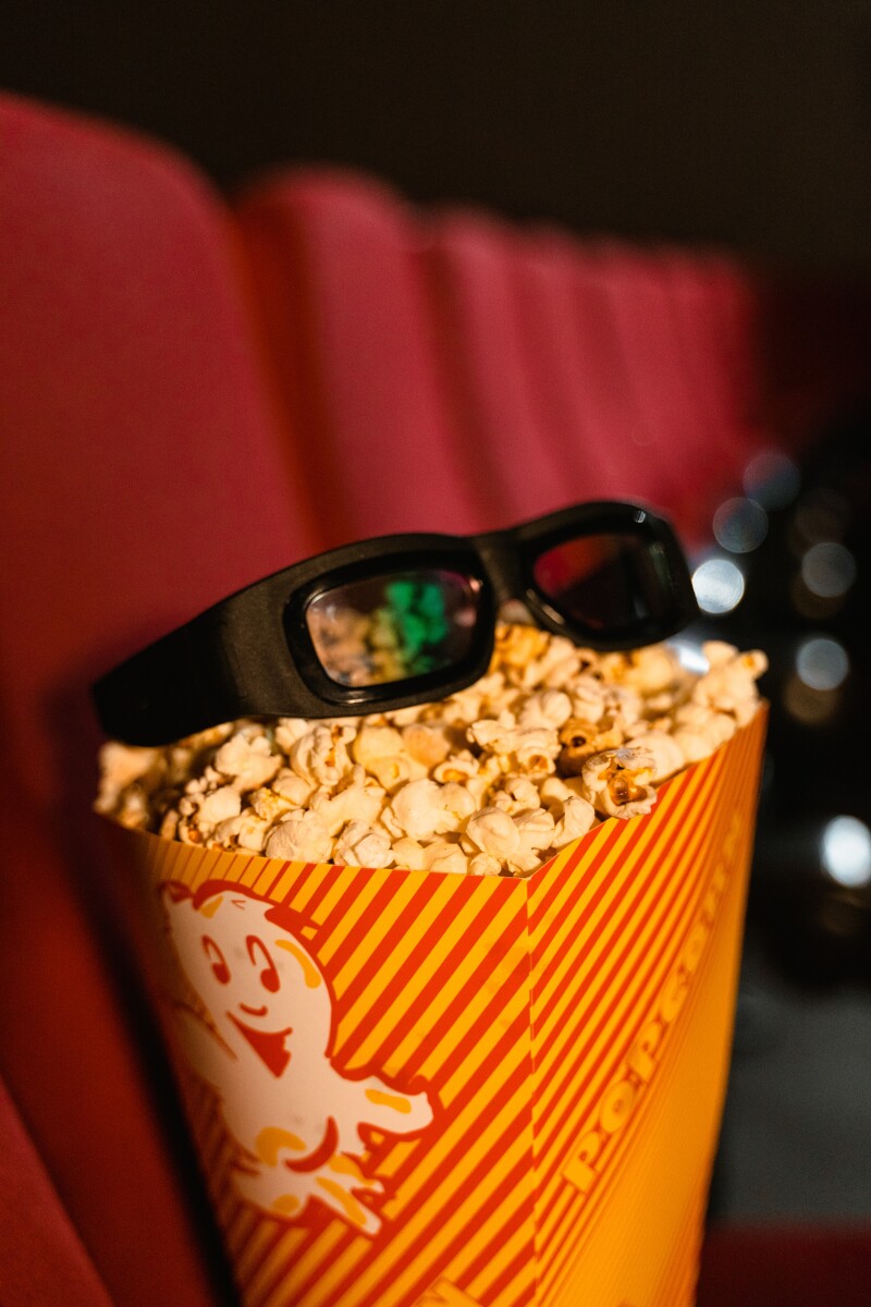 A red and white striped carton of popcorn with a pair of glasses on top.