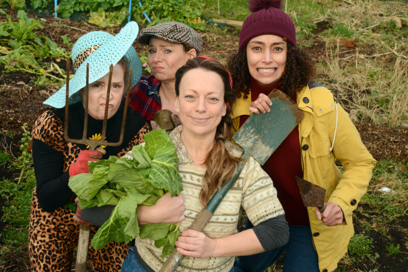 Four ladies stand in an area outside holding various gardening equipment.