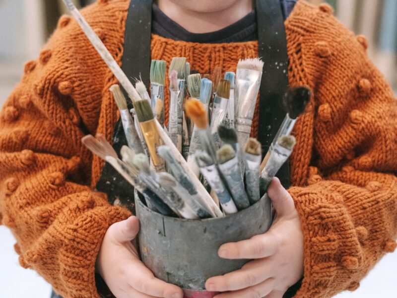 A child holding a tin full of paintbrushes.