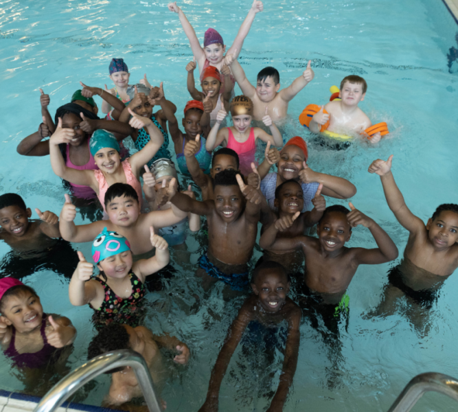 A group of young people looking happy stood up in a swimming pool.