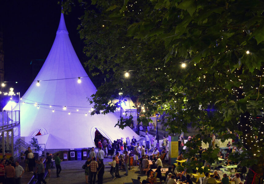 The tent lit up in festival square at Manchester International Festival at night.