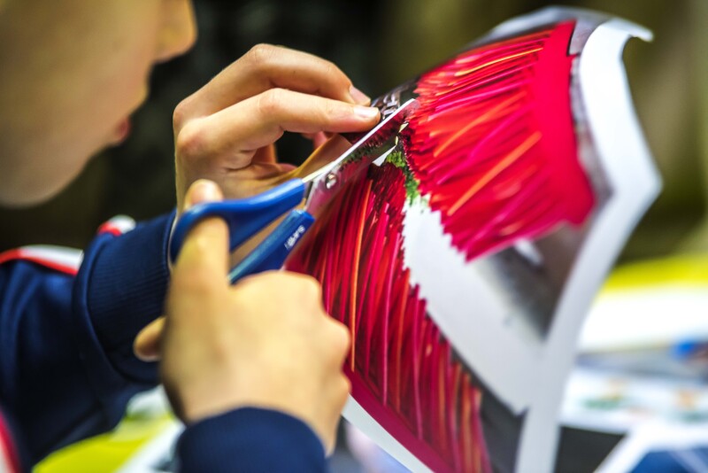 A child uses a pair of scissors to cut red paper fringing.