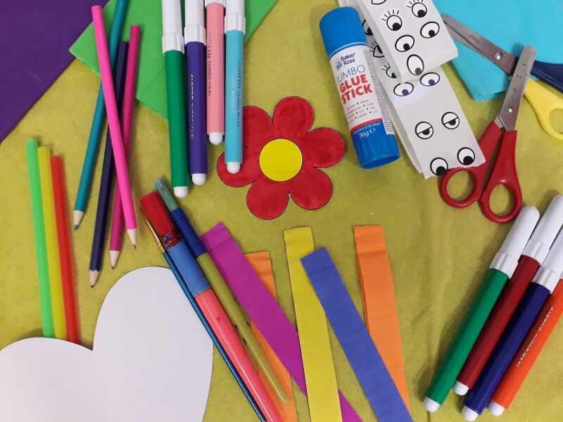 A craft table with lots of crafting materials like felt tips, glue sticks, pencils and different coloured card.